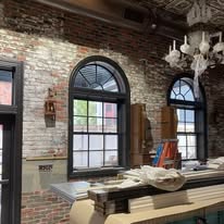 Renovated interior featuring exposed brick walls, large arched windows, and a chandelier, highlighting a blend of modern and historic design elements.