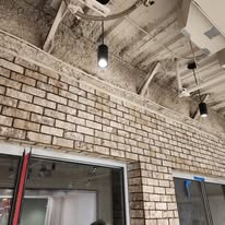 Exposed brick wall in an industrial-style space with modern lighting fixtures, showcasing a blend of rustic charm and contemporary design elements.